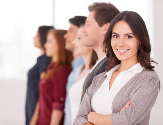 Confident leader. Attractive young woman holding arms crossed and smiling while group of people standing behind her in a row