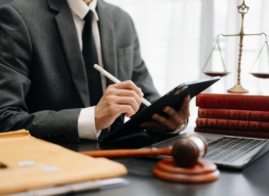 justice and law concept.Male judge in a courtroom  the gavel, working with smart phone and laptop and digital tablet computer on wood table in morning light