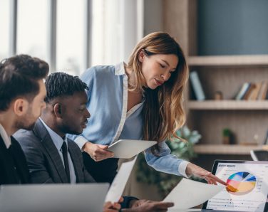 Three confident business people analyzing marketing data and using laptop while working in office together